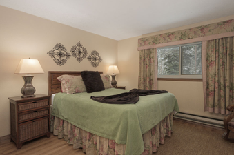 The comfortable bedroom at Beaver Village 1514 features a queen-sized bed with floral and green bedding, two nightstands with lamps, and a window with a snowy exterior view.