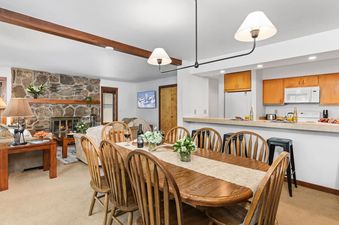 An inviting open-concept dining and living space at Sundance Jackson Hole featuring a large wooden table and a cozy stone fireplace.