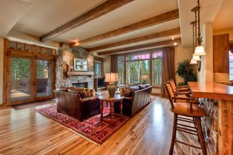 A luxurious living room in Cowboy Heaven Luxury Suite Unit 2B with a stone fireplace, leather sofas, and large windows overlooking a forest.