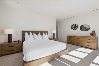 Solaris 6DE bedroom features a large bed, a dresser, two nightstands with lamps, a neutral color scheme, and plenty of natural light.
