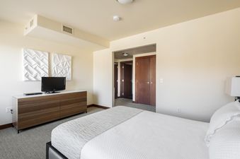 A serene bedroom at Lowell 201A featuring a large bed with white linens, a wooden dresser with a television, and two white geometric art pieces on the wall.