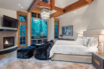 A luxurious bedroom at Silver Creek Lodge featuring a king-size bed, fireplace, plush seating area, and large windows with an outdoor view.