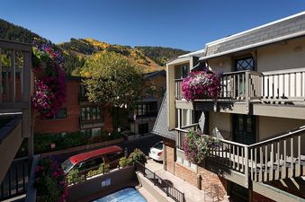 A beautiful view from the Chateau Chaumont Unit 9 balcony, featuring vibrant flowers, classic architecture, and a stunning mountain backdrop with fall colors.