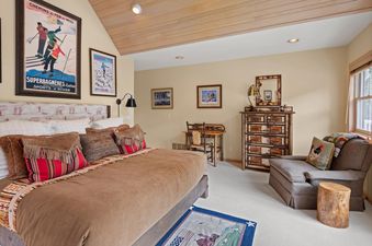 A cozy bedroom with a large bed, rustic furniture, and vintage ski posters on the walls, bathed in natural light from a window.