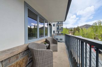 Lodge Tower 278 2BR features a private balcony with two wicker chairs, a small table, and a view of the mountainside.