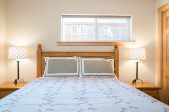 A king-size bed with a wooden headboard, two bedside tables with lamps, and a wide window above the bed.