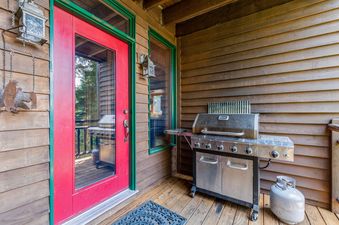 An outdoor grilling area at Cottonwood 204 with a stainless steel BBQ grill, a red door, and wooden siding.