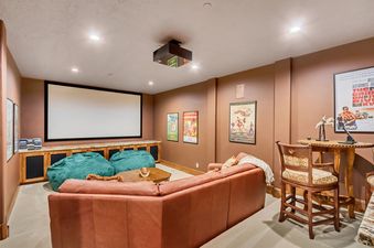 Cozy home theater room in The Lookout Home with a large projector screen, leather sectional, bean bag chairs, and movie posters.