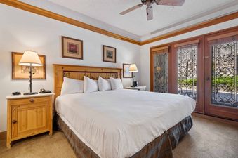 The master bedroom at The Charter F2105 features a king-size bed with white bedding, wooden nightstands, and French doors with leaded glass leading to an outdoor view.