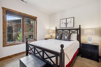 A cozy bedroom at Whitefish Ski Haus featuring a queen-sized bed with rustic decor, wooden nightstands with lamps, and a large window with a view of the outdoors.