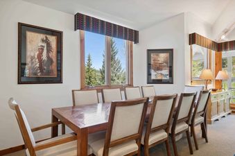 The dining room in Kiva 428 features a large, wooden table with seating for eight.  The table has a rich, dark brown finish and is surrounded by chairs with beige cushions.  The room is decorated with large, framed paintings and has windows