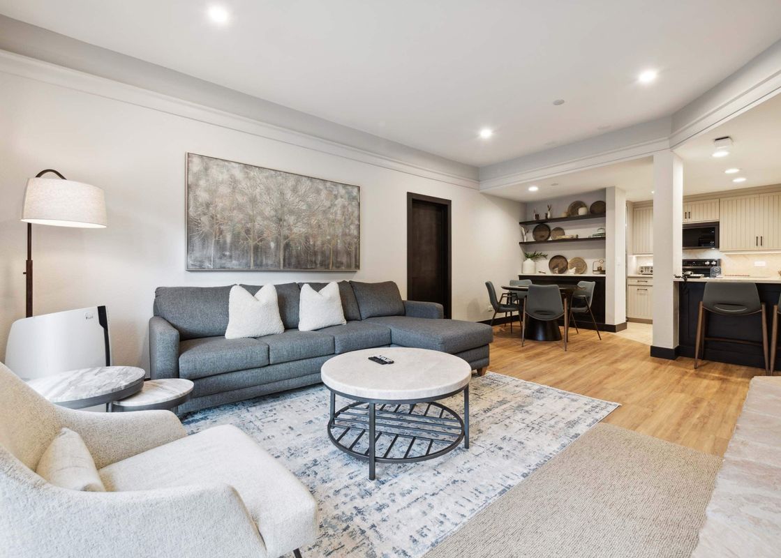 An expansive open-concept living area at The Charter D3105, featuring a gray sectional, cream armchair, dining nook, and a modern kitchen with light cabinetry.
