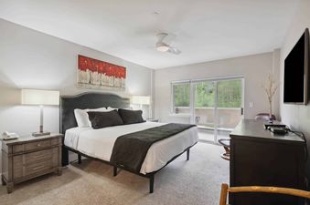 A master bedroom at St James Place 333 2BR with a king-sized bed, dark wood furniture, and a balcony overlooking a lush, green landscape.