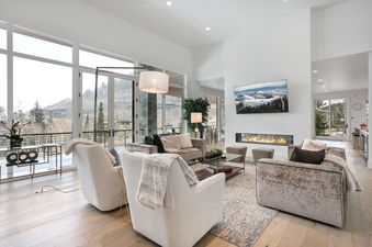A spacious and modern living room at Quicksilver Haus with large windows overlooking a snowy mountain landscape, a fireplace, and comfortable seating.