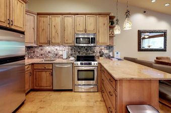 A modern kitchen in Terracehouse 64 with light wood cabinetry, stainless steel appliances, granite countertops, and a tile backsplash.