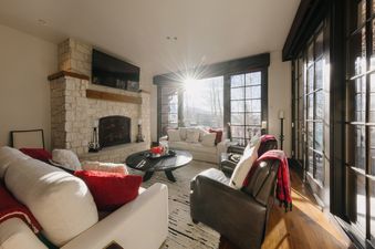A cozy living room at Ivory Stone Chalet at See Forever, featuring white sofas, a stone fireplace, and large windows with mountain views.