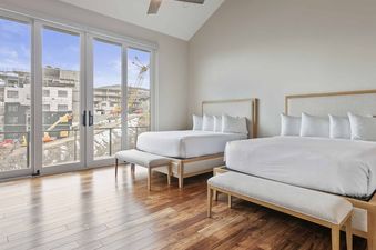 Modern bedroom with two queen beds, hardwood floors, and large glass doors opening to a balcony with mountain views.