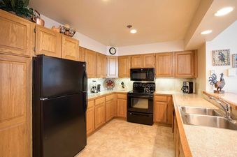 A fully equipped kitchen in Chateau Chamonix CX142, featuring wooden cabinetry, black appliances, and ample counter space with a double sink.
