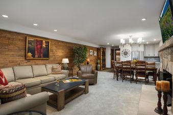 A cozy and open-concept living area with a sofa, armchair, coffee table, dining table with chairs, and a modern kitchen.