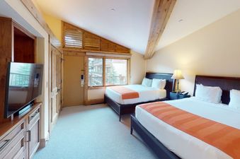 A hotel room with two double beds, a TV, and a view of a wooded area.