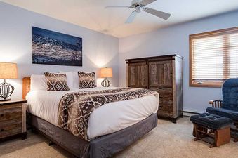 The king bedroom features a comfortable bed with rustic furnishings and a cozy armchair, ideal for relaxation at Pines Condominiums Two Bedroom.