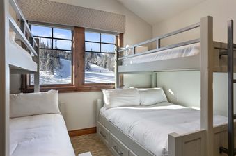Grand Lodge 5 Bedroom Penthouse 504 bedroom features two sets of bunk beds with white linens and pillows, one set with a window view of a snowy mountain.