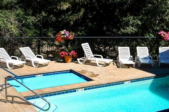 SunRiver includes an outdoor pool with a small hot tub, lounge chairs, and lush trees surrounding the property.