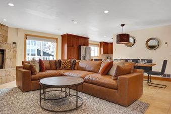 A spacious living room in Resort Plaza 5043 with a brown leather sectional, a round coffee table, and a view of the adjacent kitchen and dining area through a large window.