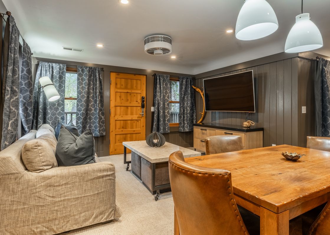 The comfortable and functional lounge and dining area in Cedar Crest Osprey Cottage 3 features a sofa, a dining table with chairs, a television, and elegant decor.