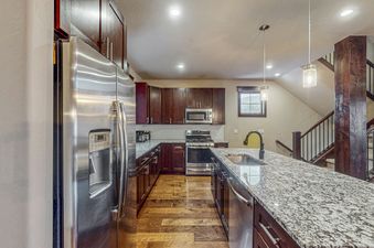 A modern kitchen in the Keystone Townhome features dark wood cabinetry, stainless steel appliances, a large granite island with a sink, and pendant lighting.