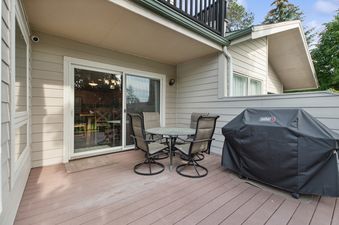 The private deck at Tee Time features an outdoor dining set with a round table and four chairs, alongside a Weber BBQ grill.