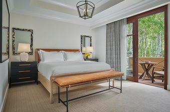 A spacious bedroom in the Montage Three Bedroom Residence Resort View features a king-sized bed with white linens, dark wood nightstands, and a private balcony overlooking a lush forest.