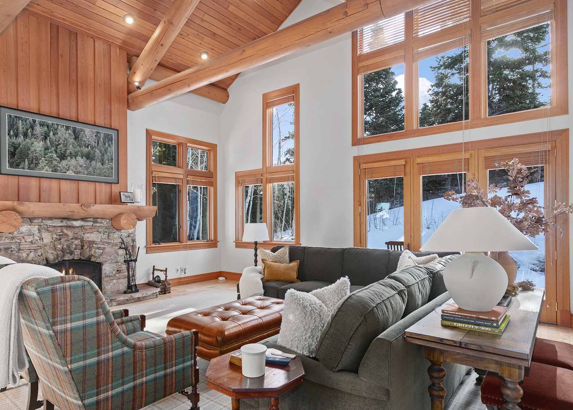 A spacious and cozy living room at 7780 Sterling Drive features a stone fireplace, comfortable seating, and large windows with views of a snowy landscape.