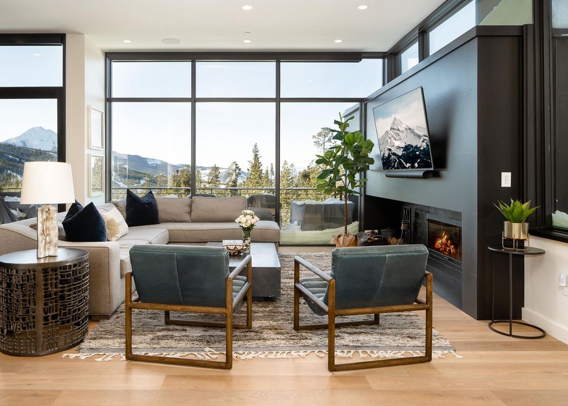 The living room of Moonlight Basin 6A Treeline Springs has a fireplace with a roaring fire, comfy leather seating, and an expansive view of the snow-capped mountains.