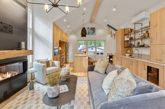 A modern open-concept living room and kitchen with a grey sofa, fireplace, and light wood cabinetry.