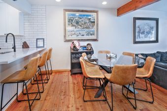 A dining room with a glass table, leather chairs, and a bar area with stools.