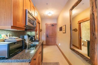 A small kitchen in a condo with stainless steel appliances, a granite countertop and wooden cabinets.