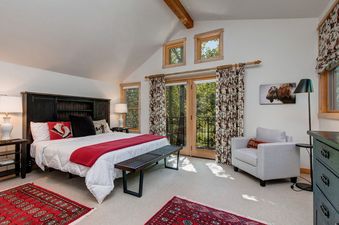 A bedroom with a king-sized bed, a large window with a view of trees, and a white armchair.