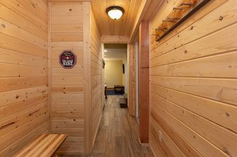 The hallway at 8 Crown Drive features light wood paneling, a coat rack with five pegs, and a decorative sign that reads "Welcome Skiers Un-load Here" above a wooden bench.