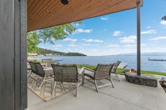 A waterfront patio at the Swan Lake House with comfortable seating, a wooden ceiling, and a stunning view of the lake and surrounding landscape under a clear sky.
