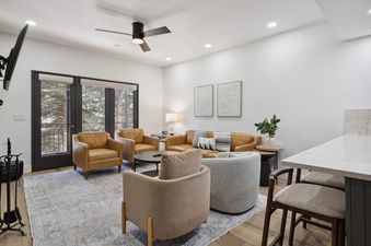 A luxurious and spacious lounge at The Charter G1205, featuring leather and fabric armchairs, a large leather sofa with decorative pillows, a round coffee table, and glass doors opening to a winter balcony view.