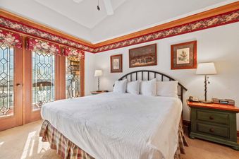 A cozy bedroom featuring a king-sized bed with white linens, flanked by dark green nightstands with lamps, and adorned with floral valances over windows.
