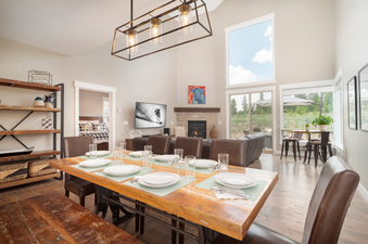 The dining area and living room with a fireplace, television, and outdoor views are featured in the Alder Brook Homers Hideaway.