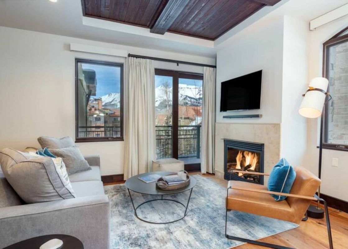 The living room of Lumiere One Bedroom Standard Residence, with a fireplace, large windows, and a view of the mountains.