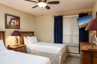 A guest bedroom in Montaneros 312 with two twin beds, a Kokopelli lamp, and a framed painting of horses.