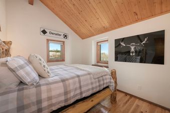 A cozy bedroom in Kings Crossing townhome 13 features a wooden bed frame, plaid bedding, and a moose artwork.