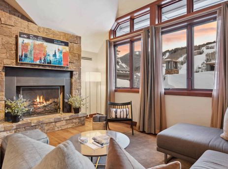 A living room with a fireplace, a couch, and a view of a snowy mountain.