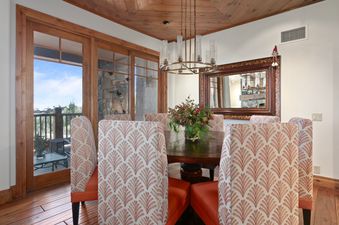 Dining room with a large wooden table and chairs with floral patterned upholstery, a chandelier, and a mirror on the wall.