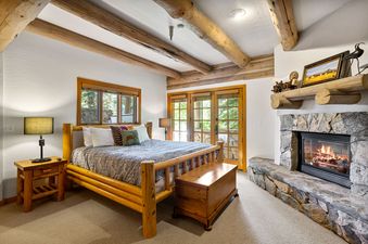 A cozy bedroom at Pine Inn 1 at Trails End Lodge, with a wood-burning fireplace, a king-sized bed, and a wooden chest at the foot of the bed.