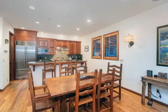 A dining table with wooden chairs and a fully equipped kitchen with stainless steel appliances and wood cabinetry are the focal points of the integrated dining area and kitchen at South Pacific Townhouse.